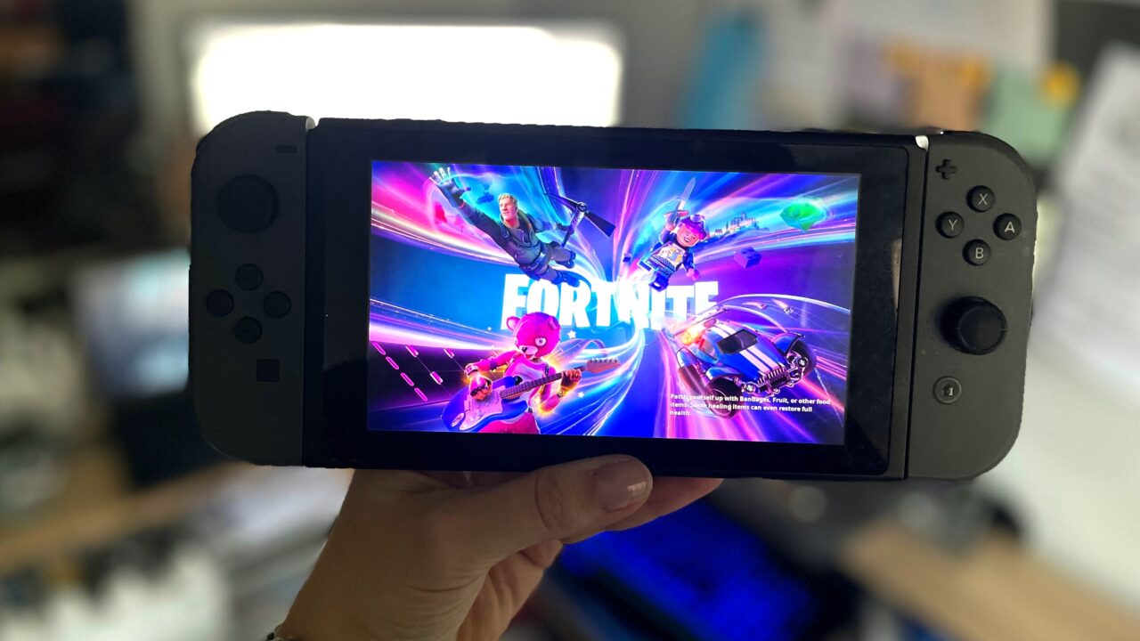 Ręka trzymająca przenośną konsolę do gier Nintendo Switch z ekranem wyświetlającym ekran startowy gry Fortnite.