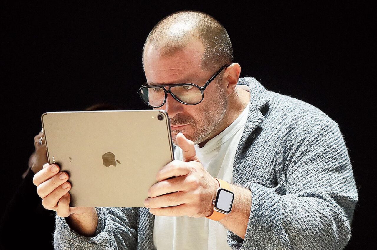 Jony Ivew okularach koncentruje się na przeglądaniu zawartości na tablecie, który trzyma obiema rękami. 