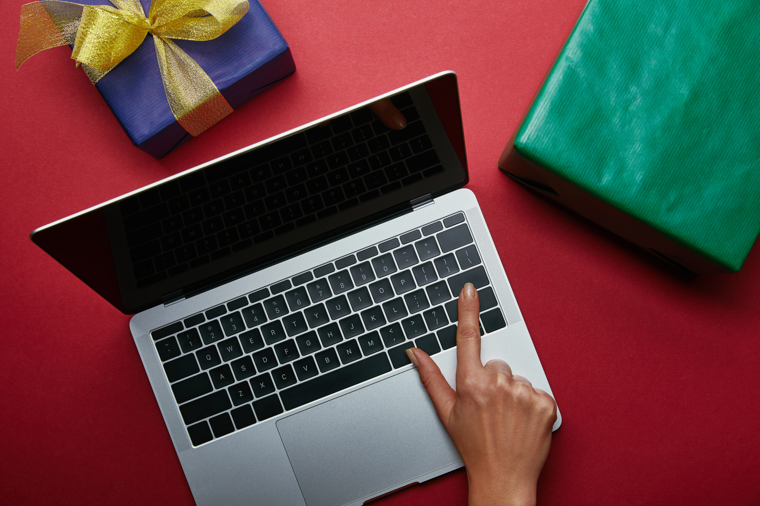 Osoba używa laptopa umieszczonego obok prezentów na czerwonym tle.