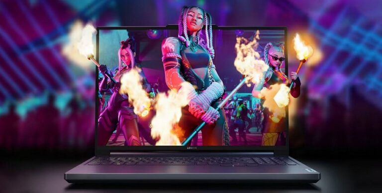 Laptop gamingowy marki Legion stojący na stole z wyświetlonym żywym obrazem przedstawiającym trzy wojowniczki z gry, które wydają się "wyskakiwać" z ekranu z ognistymi efektami w rękach, na tle abstrakcyjnego, kolorowego oświetlenia.