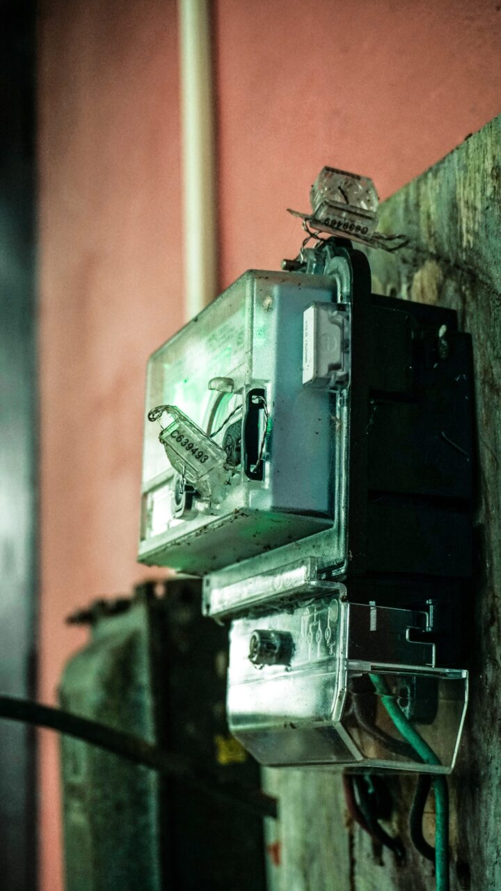 Stare metalowe skrzynki elektryczne z widocznymi przewodami i bezpiecznikami zamocowane na ścianie w półmroku.