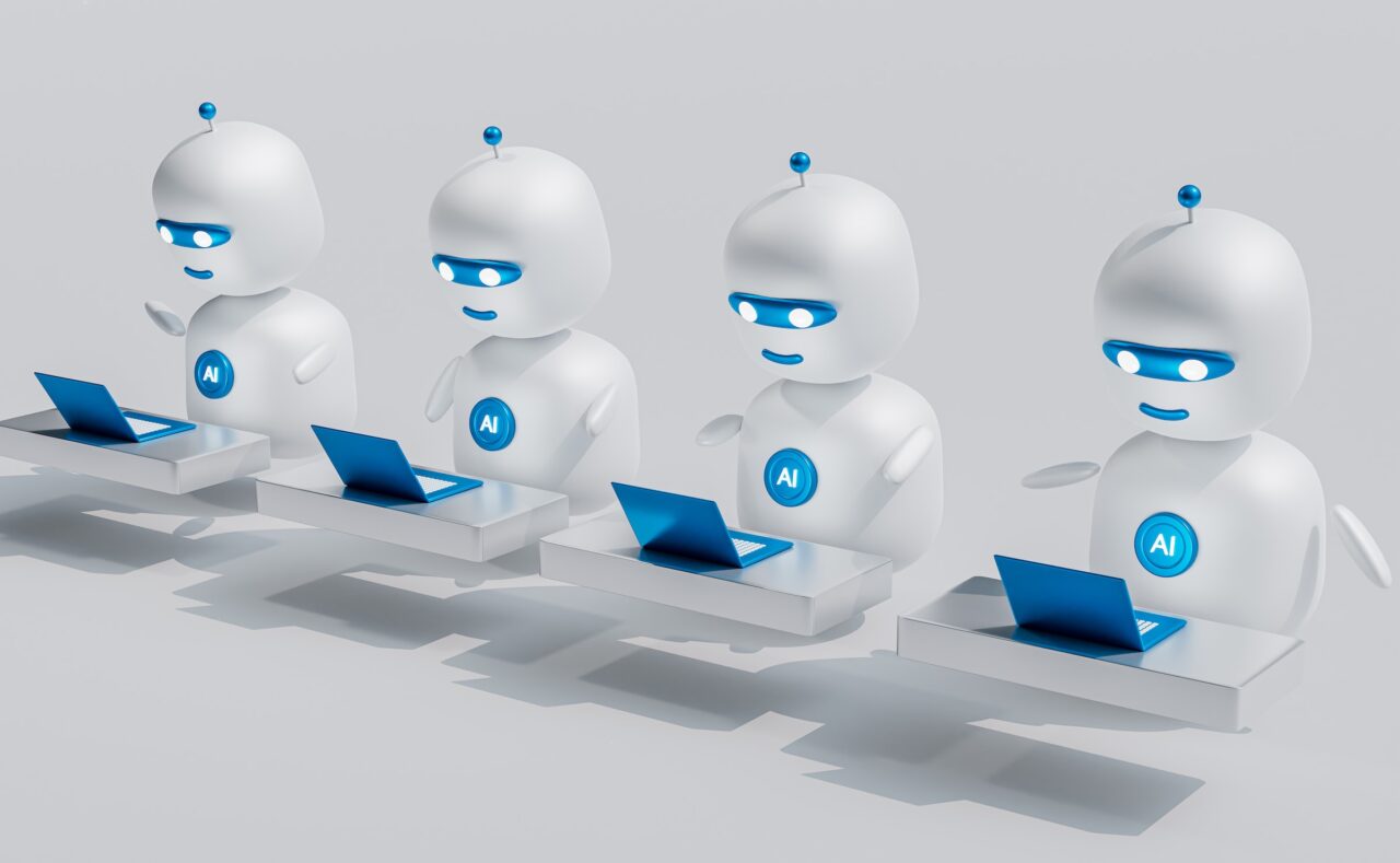 chatbot AI - Czterech animowanych robotów o wyglądzie antropomorficznym siedzących przy biurkach i korzystających z laptopów, z oznaczeniem "AI" na ich tułowiach i na ekranach laptopów; tło jest jednolite, szare.