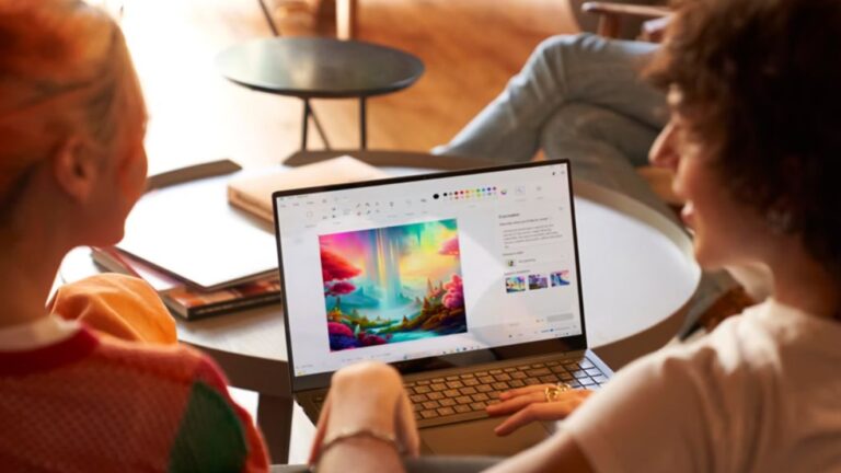 Dwie osoby pracujące na laptopie z kolorową grafiką na ekranie w jasnym wnętrzu.
