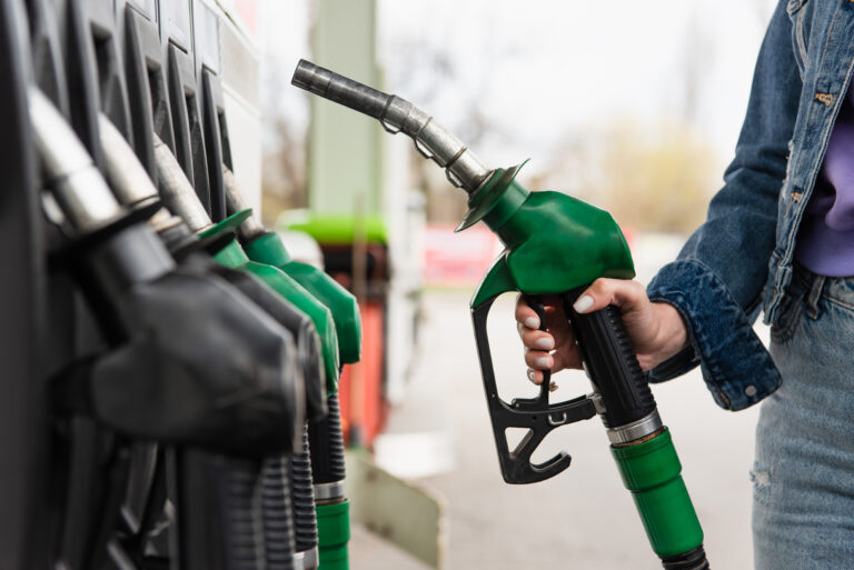 Osoba trzymająca zieloną pistoletową końcówkę dystrybutora paliw E10 na stacji benzynowej.