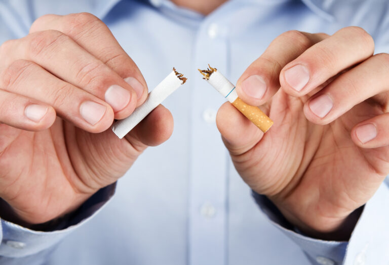 Osoba łamie papierosa na pół, symbolizując rzucenie palenia.