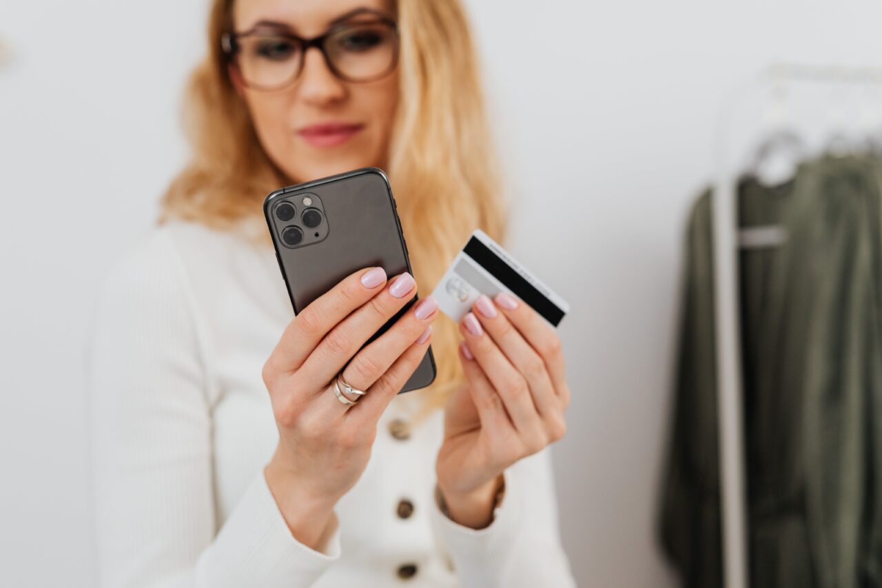 Kobieta, do której mogli dzwonić oszuści bankowi, w okularach trzyma smartphone i kartę kredytową.