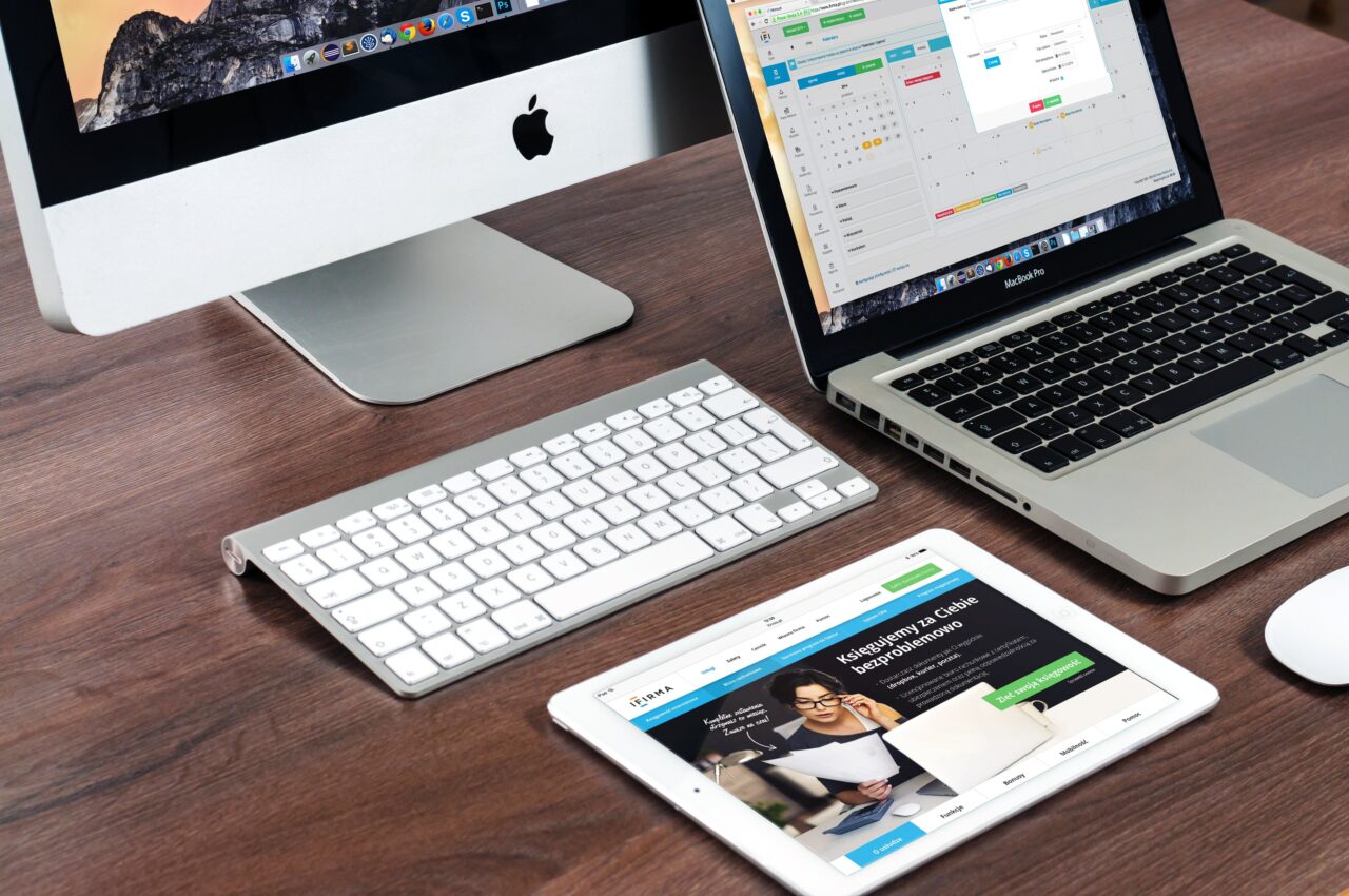 Biurko z komputerem iMac, laptopem MacBook Pro i tabletem iPad pokazującym stronę internetową, a także klawiaturą i myszą Apple.