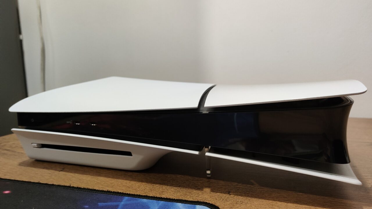 Konsola do gier PlayStation 5 umieszczona na biurku, o białym, futurystycznym designie z czarnymi akcentami.