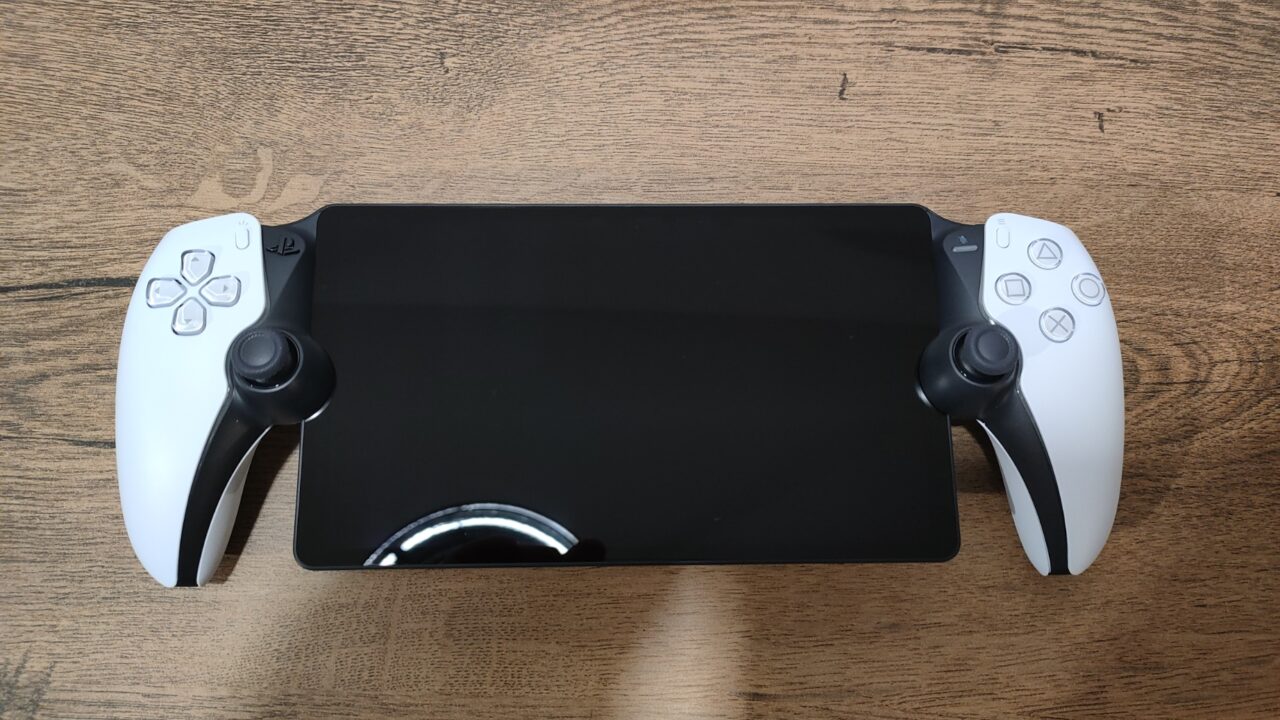 Podłączony do czarnej przenośnej konsoli do gier PlayStation Portal kontroler w biało-czarnej kolorystyce na drewnianym tle.