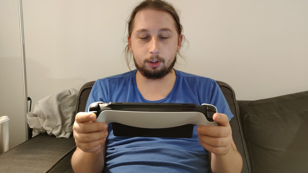 Mężczyzna siedzący na kanapie, grający na przenośnej konsoli do gier PlayStation Portal