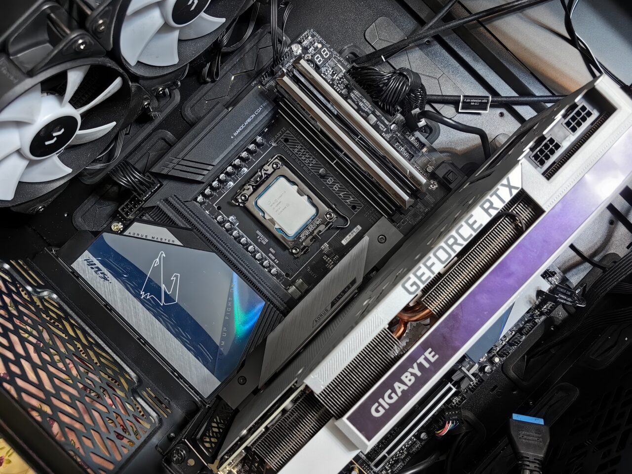 Wnętrze komputera z widocznym procesorem, częścią chłodzenia wodnego, kartą graficzną GeForce RTX, pamięcią RAM oraz innymi komponentami na płycie głównej.