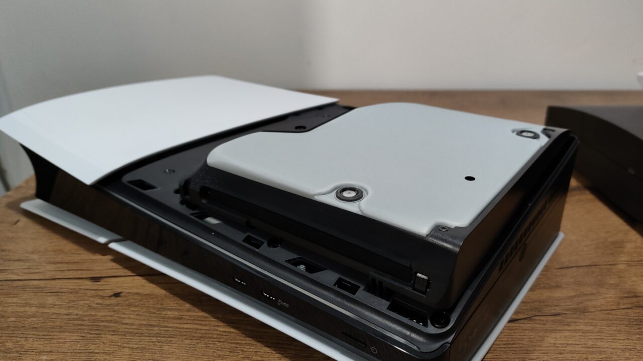 Częściowo otwarta biała konsola do gier PlayStation 5 Slim z widocznymi portami USB i przyciskami na przednim panelu, postawiona na drewnianym biurku.