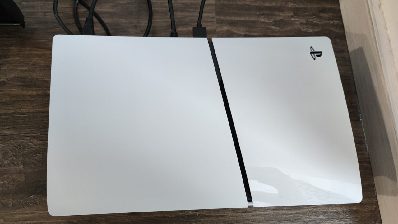 Dwa leżące obok siebie białe panele konsoli do gier PlayStation 5 Slim z czarną linią między nimi na drewnianym blacie.