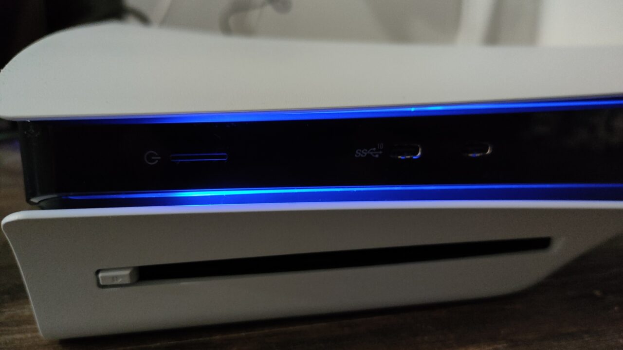 Biała konsola do gier PlayStation 5 Slim z niebieskim podświetleniem, przedstawiająca szczegół portów USB i przycisk włączania.