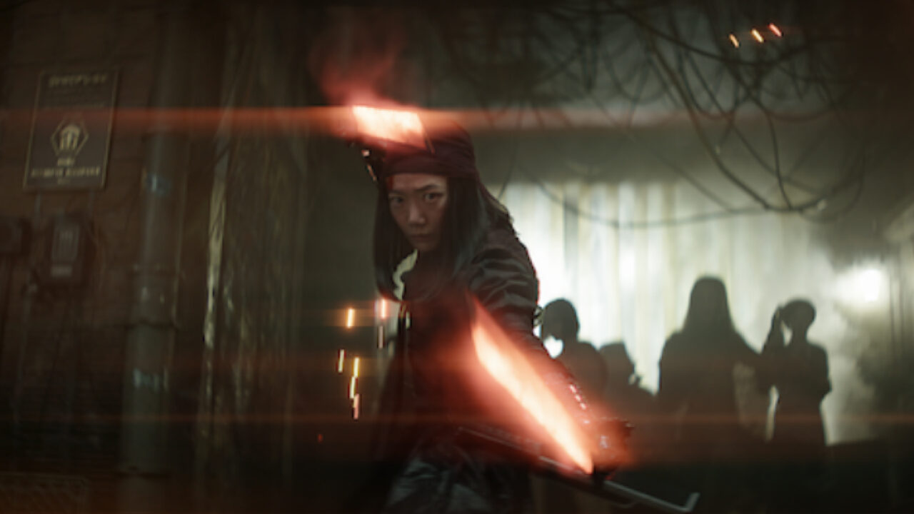 Osoba w stroju ninja trzyma świecący czerwony miecz, stojąc w mrocznym pomieszczeniu z zamglonymi sylwetkami w tle.