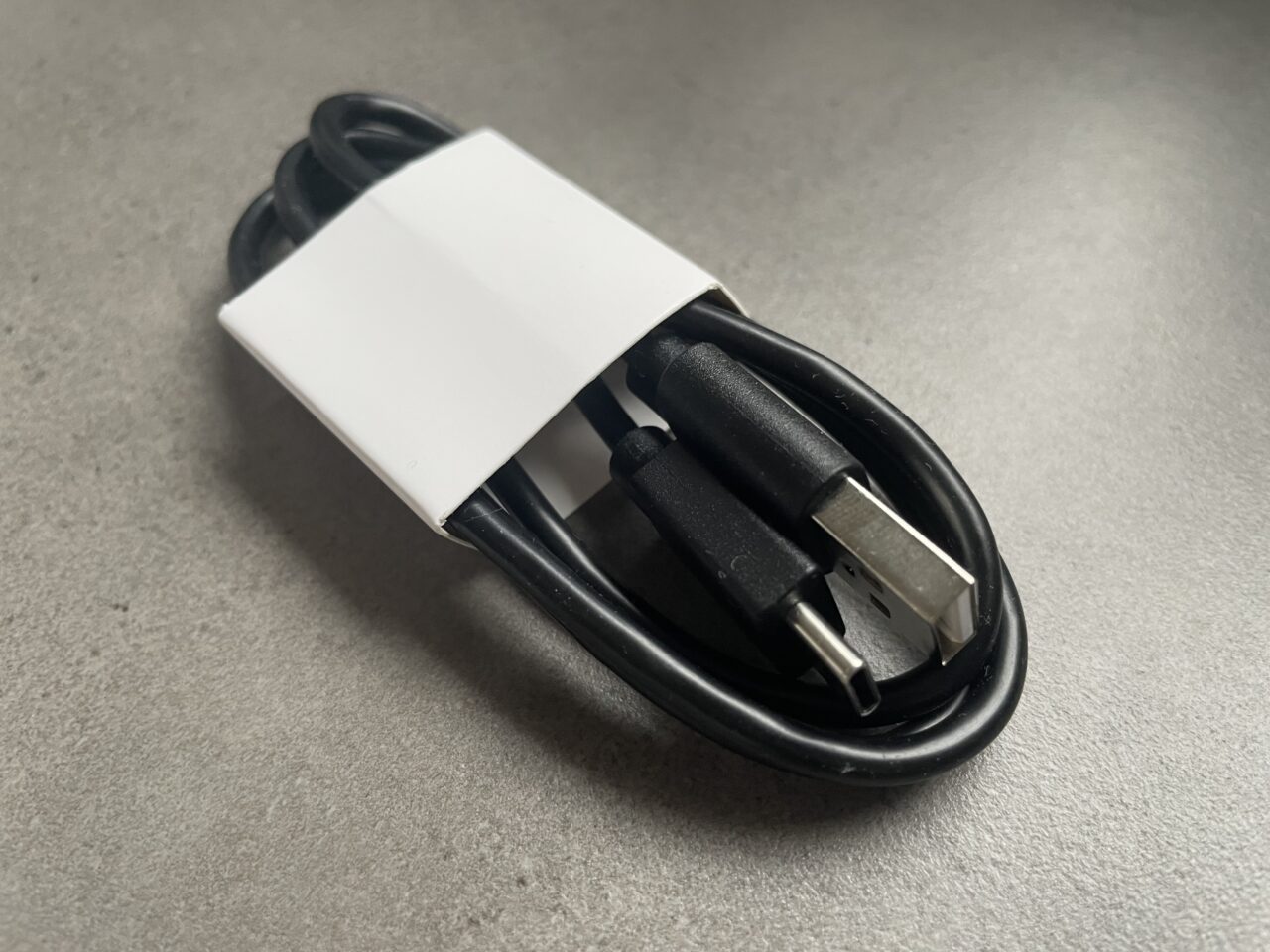 Zwinięty czarny kabel USB z białym złączem adaptera na szarym tle.
