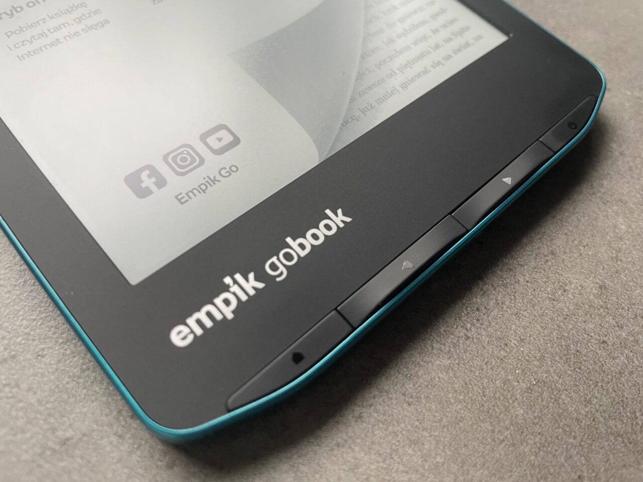 Część przedniego panelu czarnego czytnika e-booków z turkusowym obramowaniem i wyświetlonym tekstem, z widoczną nazwą produktu "empik gobook" oraz przyciskami nawigacyjnymi.