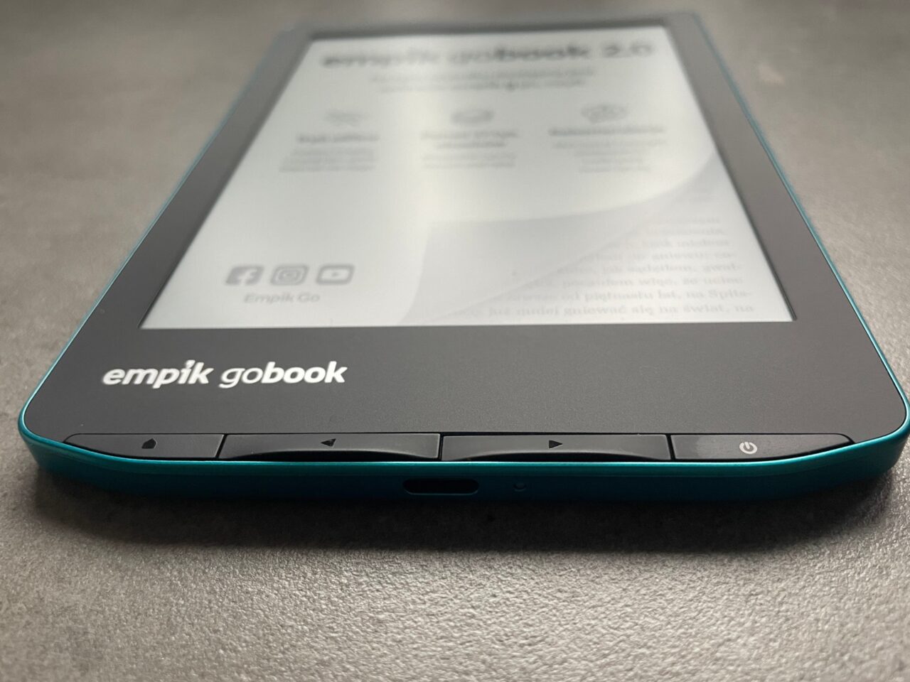 Czytnik e-booków marki Empik GoBook na szarym tle, z widocznym ekranem i częścią niebiesko-zielonej obudowy.