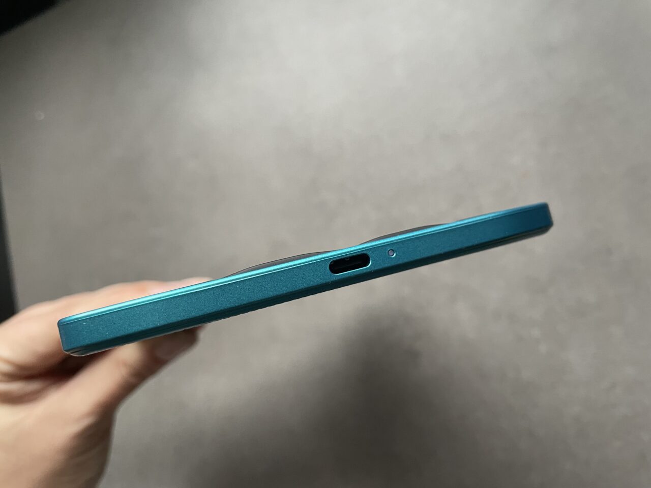 Boczny widok zamkniętego, niebieskiego laptopa z widocznym portem USB i wycięciem na wentylację.