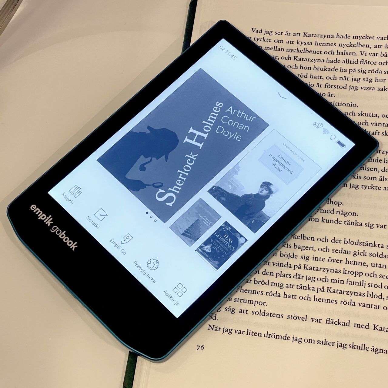 Czytnik ebooków leżący na otwartej książce wyświetla okładkę "Sherlock Holmes" Arthura Conana Doyle'a oraz interfejs użytkownika Empik Go.
