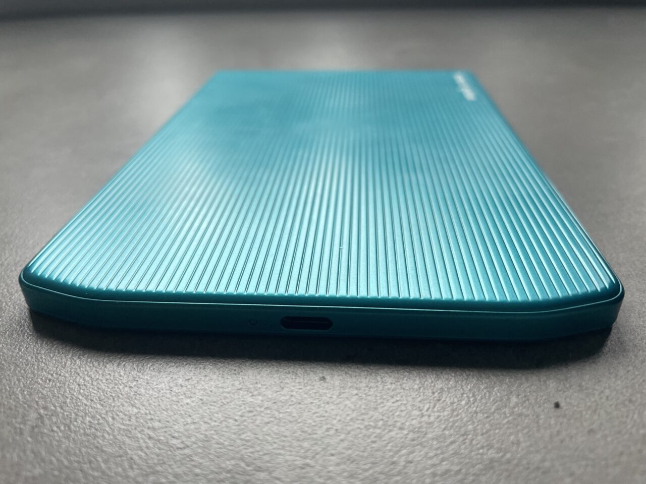 Niebieski smartfon z teksturowanym tylnym panelem, skierowany ekranem do dołu, leżący na szarym blacie.