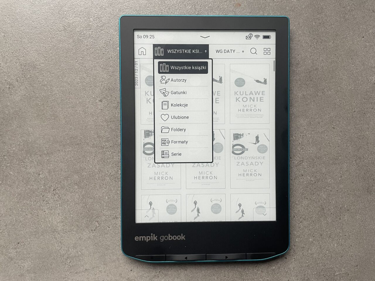 Czytnik ebooków marki Empik GoBook wyświetlający interfejs użytkownika z listą e-książek, położony na szarym tle.