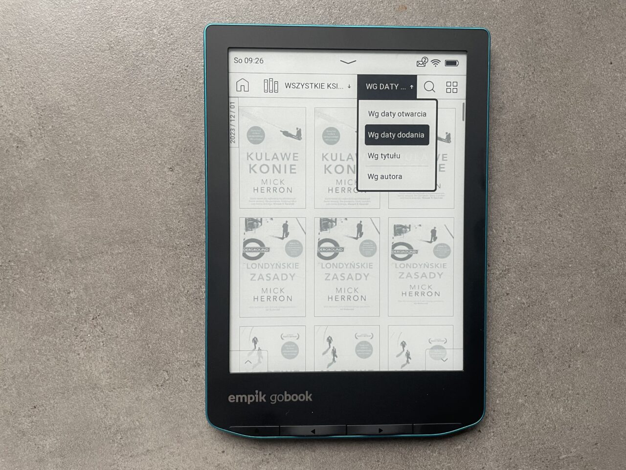 Czytnik ebooków marki Empik GoBook leżący na szarym podłożu, wyświetlający menu z opcjami sortowania książek i widocznym interfejsem użytkownika.