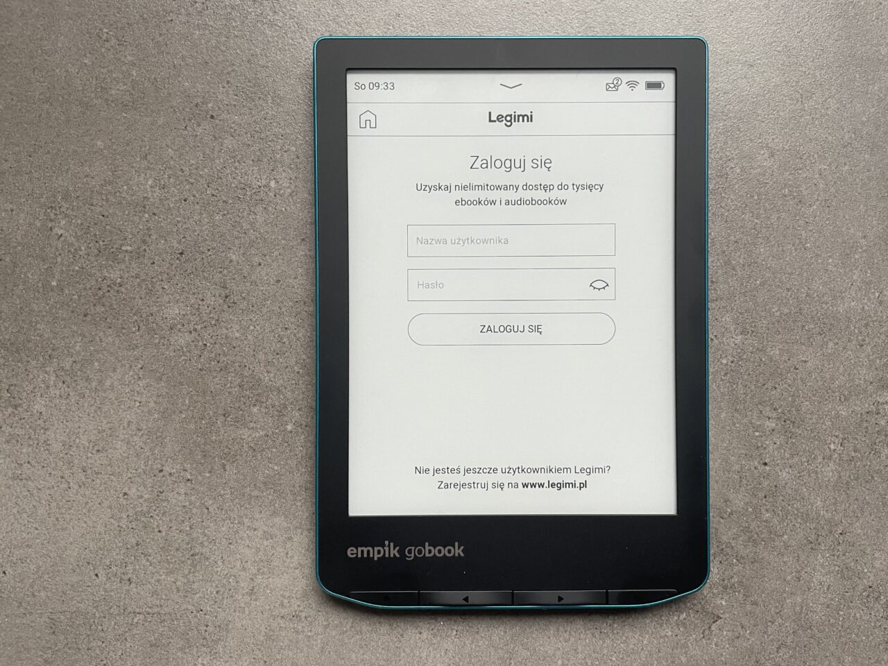 Czytnik e-booków leżący na szarym tle z ekranem wyświetlającym stronę logowania do serwisu Legimi.