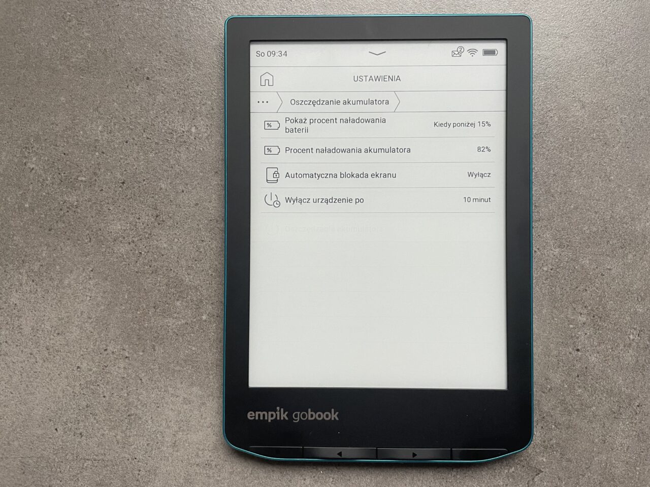 Czytnik e-booków "empik gobook" leżący na szarym blacie, z włączonym ekranem wyświetlającym menu ustawień baterii.