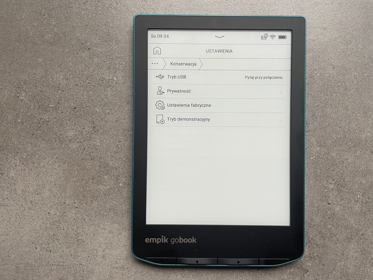 Czytnik e-booków Empik GoBook na szarym tle, wyświetlający menu ustawień z opcjami takimi jak konservacja, tryb USB, prywatność czy ustawienia fabryczne.