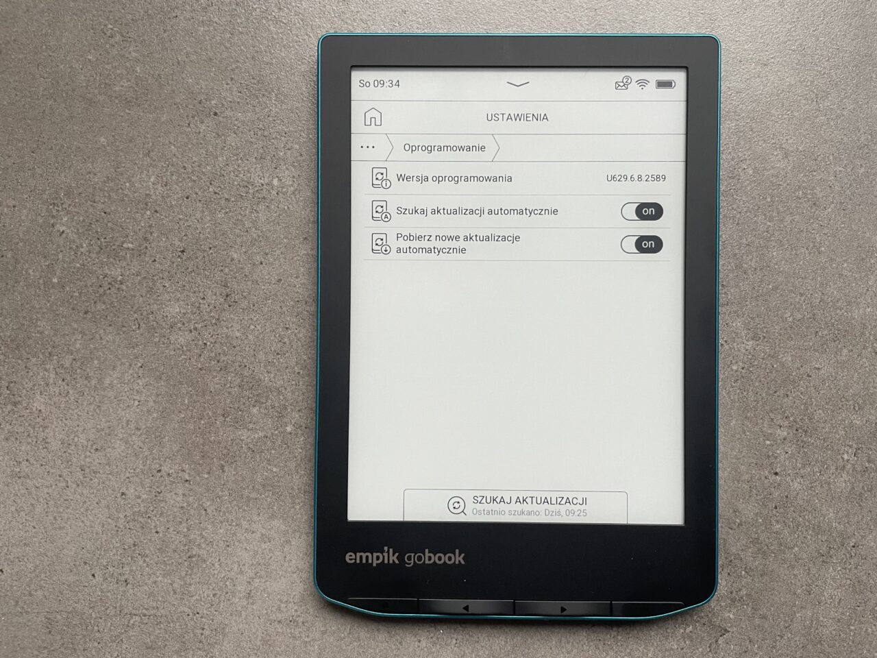 Czytnik e-booków leżący na szarym tle, z otwartym ekranem ustawień aktualizacji oprogramowania.