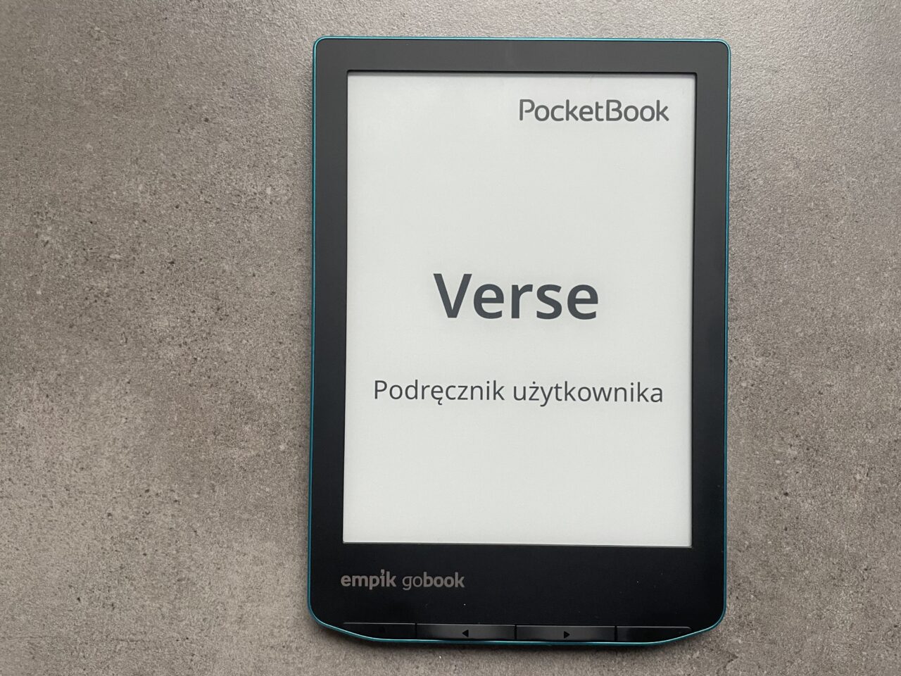 Czytnik ebooków marki PocketBook leżący na szarym blacie, wyświetlający stronę tytułową podręcznika użytkownika z napisem "Verse".