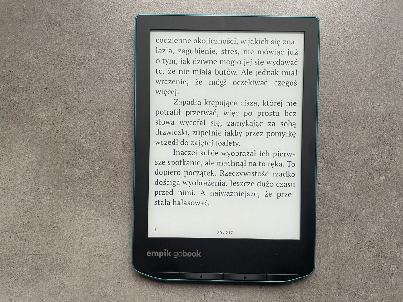 Czytnik ebooków marki Empik leżący na szarym tle, na ekranie wyświetlona strona z tekstem w języku polskim.