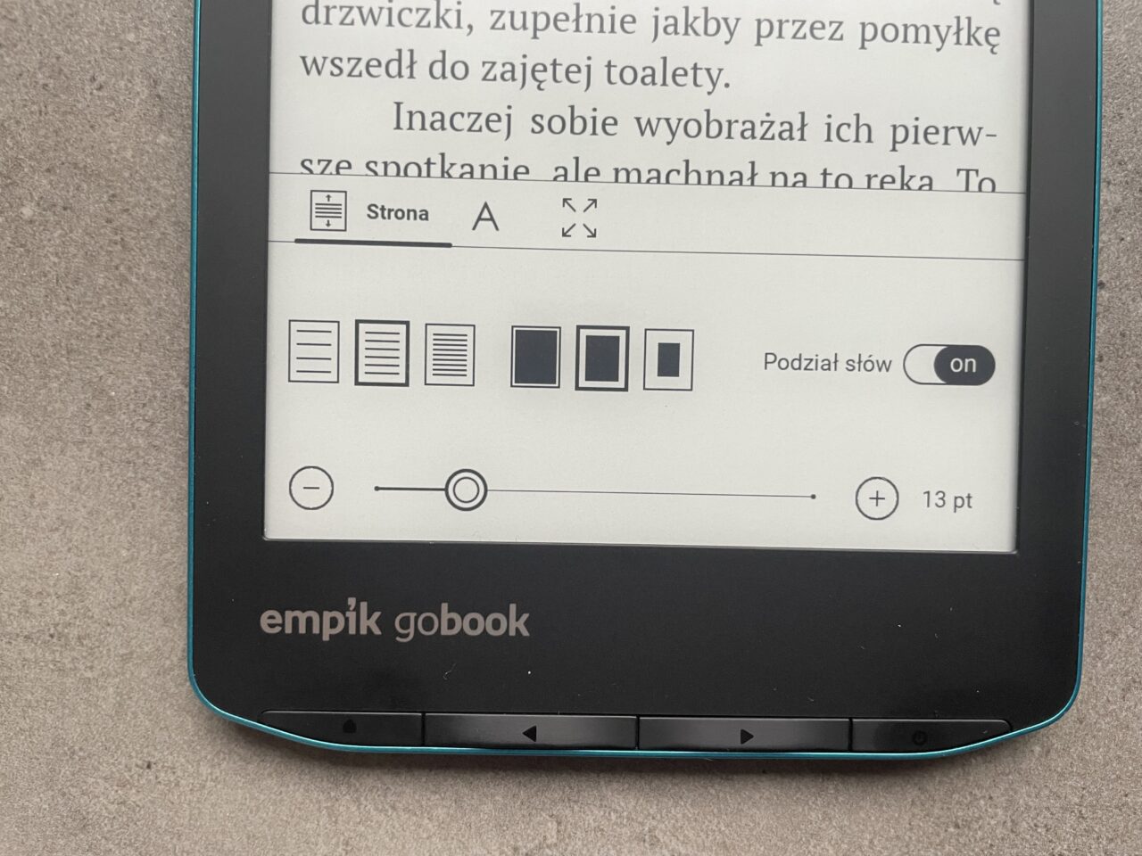 Część ekranu czytnika e-booków z tekstami i opcjami formatowania, w tle szary materiał.