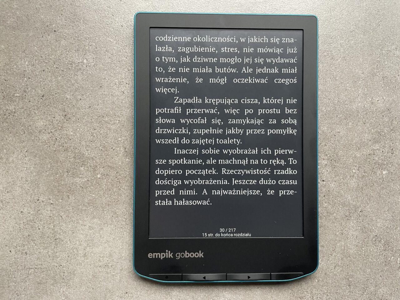 Czytnik e-booków marki Empik leżący na szarym tle, z wyświetlonym tekstem w języku polskim i widocznymi elementami interfejsu użytkownika, takimi jak numer strony i pasek postępu.