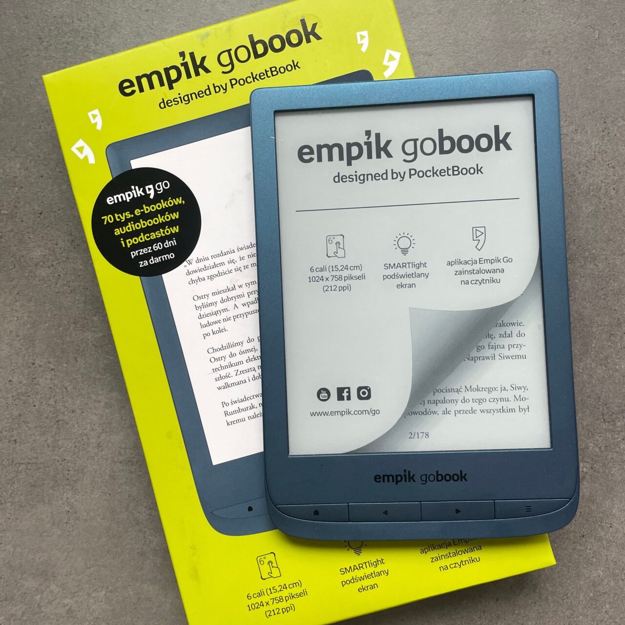 Czytnik e-booków Empik GoBook zaprojektowany przez PocketBook, leżący na opakowaniu, z widocznym ekranem startowym i informacjami o urządzeniu.