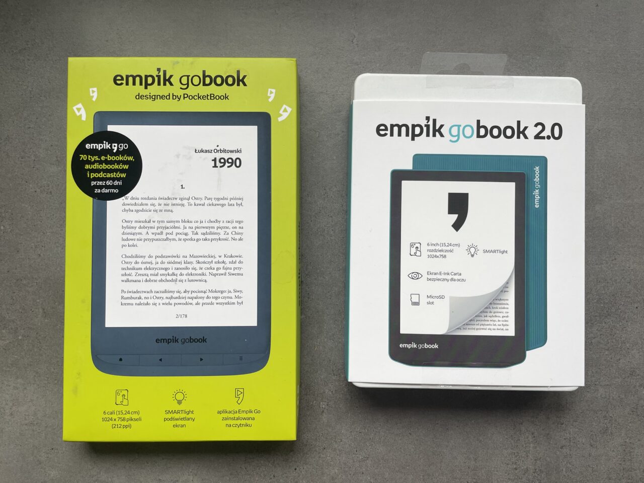 Opakowania dwóch czytników e-booków Empik GoBook i Empik GoBook 2.0 ułożone na szarym tle.