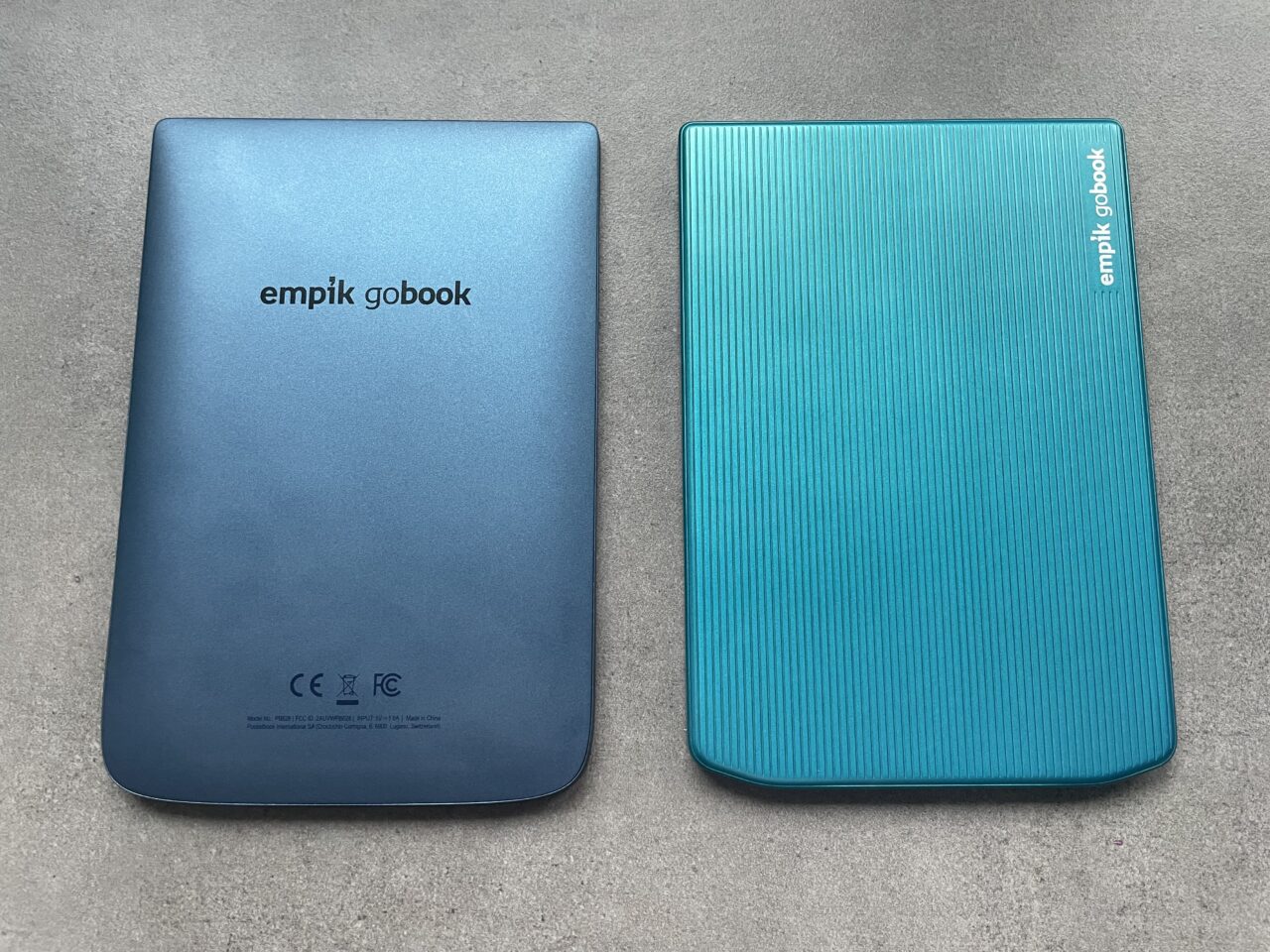 Dwa zamknięte czytniki ebooków leżące obok siebie na szarym tle; lewy w kolorze gradientu od granatu do błękitu z napisem "empik gobook", prawy w błękitnym kolorze z poziomymi żłobieniami i białym napisem "empik gobook" po boku.