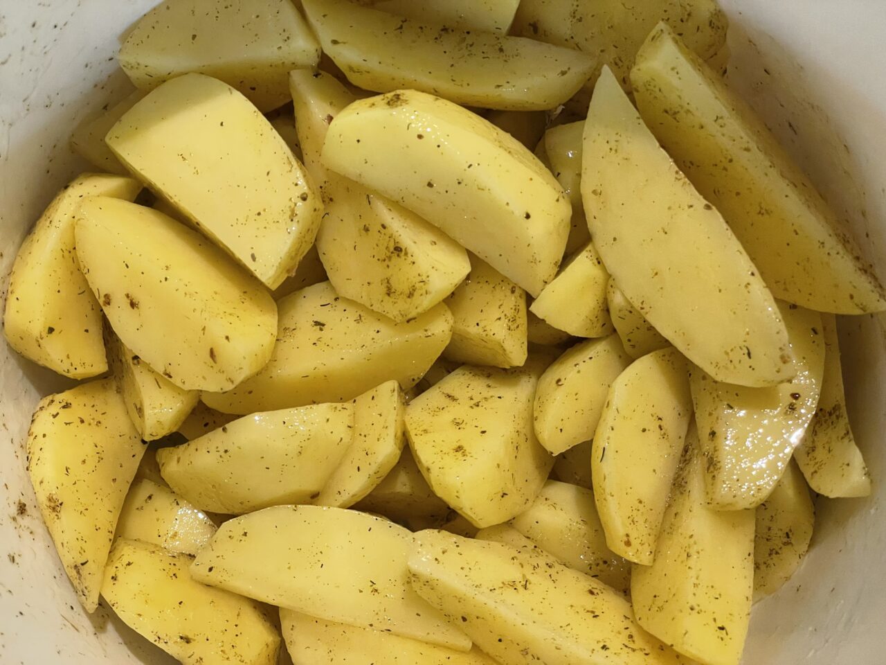 Pokrojone ziemniaki przyprawione ziołami w misce.