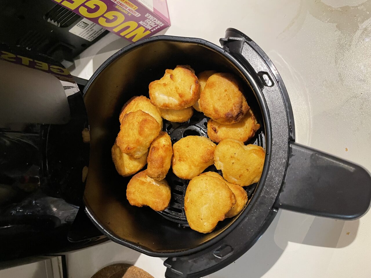 Zdjęcie przyrumienionych kawałków kurczaka w koszyku frytkownicy bezolejowej na kuchennym blacie.