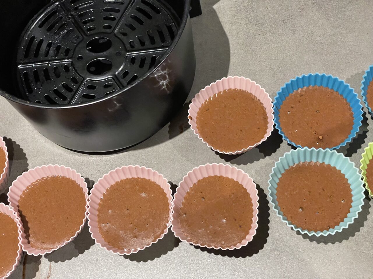 Formy do pieczenia muffinek napełnione ciastem czekoladowym ułożone obok kosza do frytkownicy na blacie kuchennym.