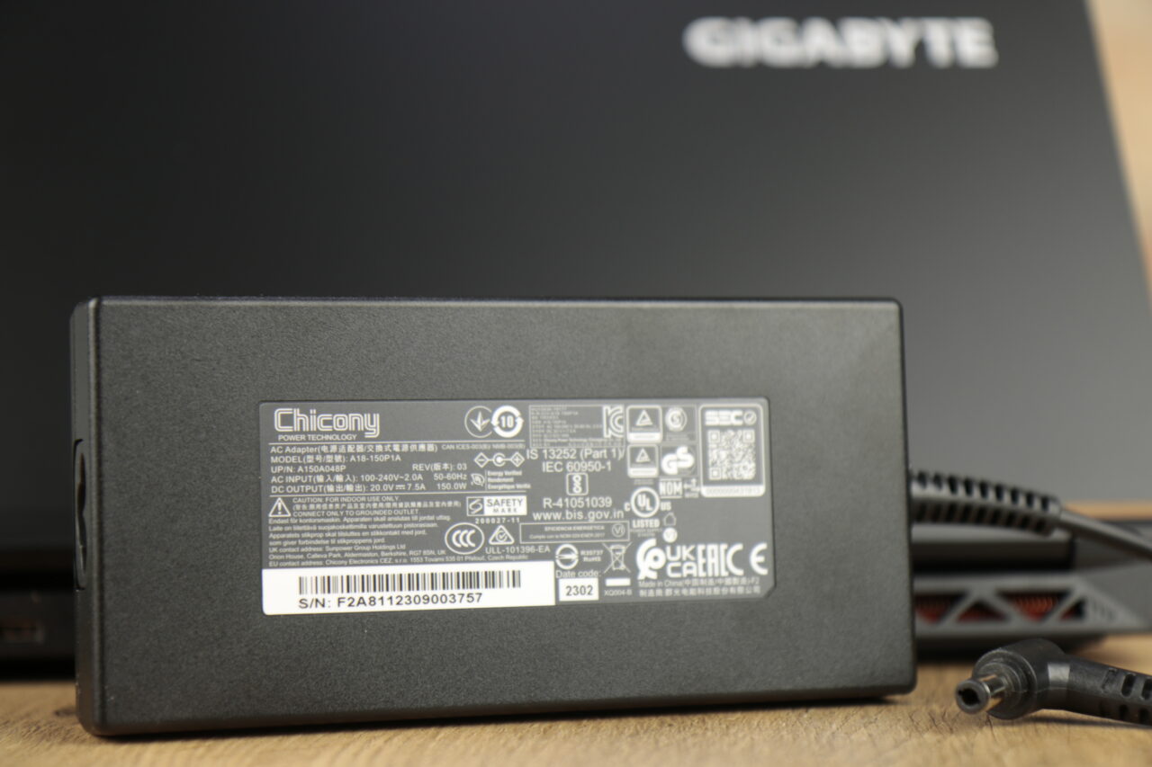 Czarny zasilacz Chicony z zestawu recenzowanego Gigabyte G5 MF z etykietą zawierającą dane techniczne, na tle pudełka z logo Gigabyte.