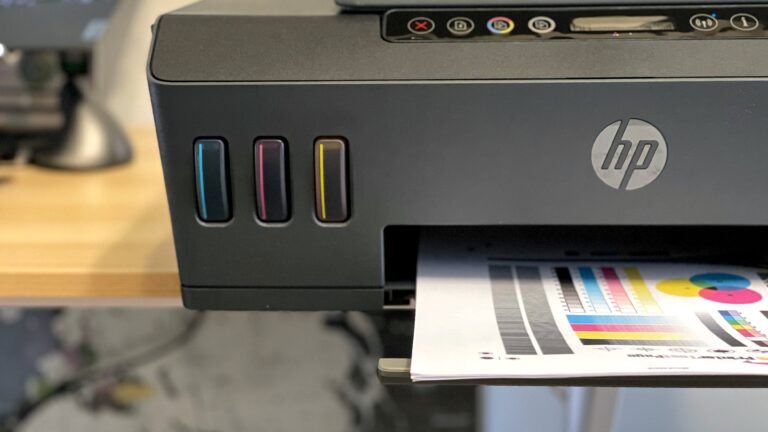 Częściowy widok drukarki HP z otwartym przedziałem na atrament i wydrukowanym testem kolorów, który jest właśnie drukowany.