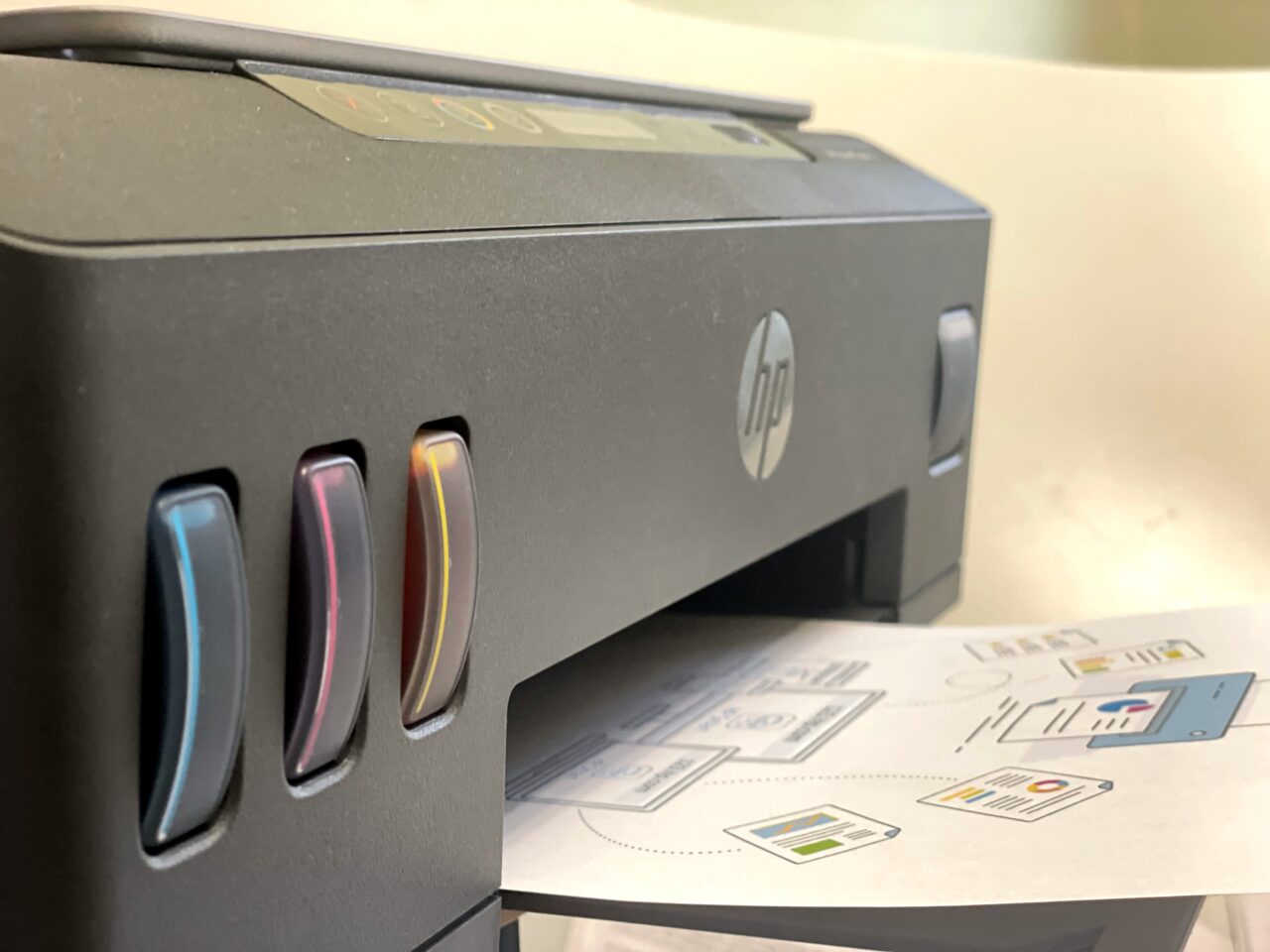 Drukarka HP z wyróżniającymi się kolorowymi wkładami tuszu na pierwszym planie, z wydrukowaną stroną z ilustracjami położoną poniżej.