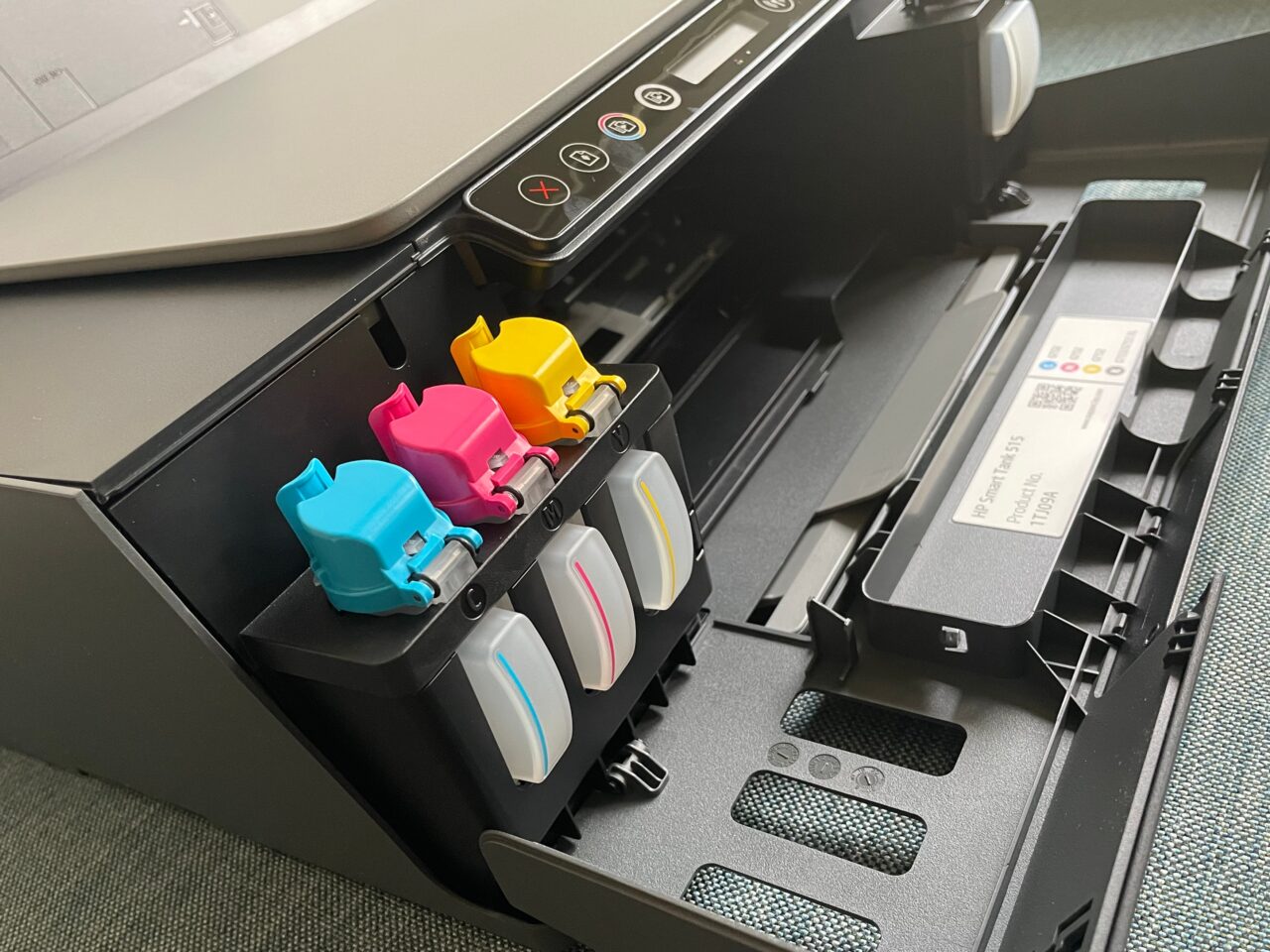 Wnętrze otwartej drukarki biurowej z widocznymi kolorowymi pojemnikami z tuszem w kolorach cyjanku, magenty, żółci i czerni.