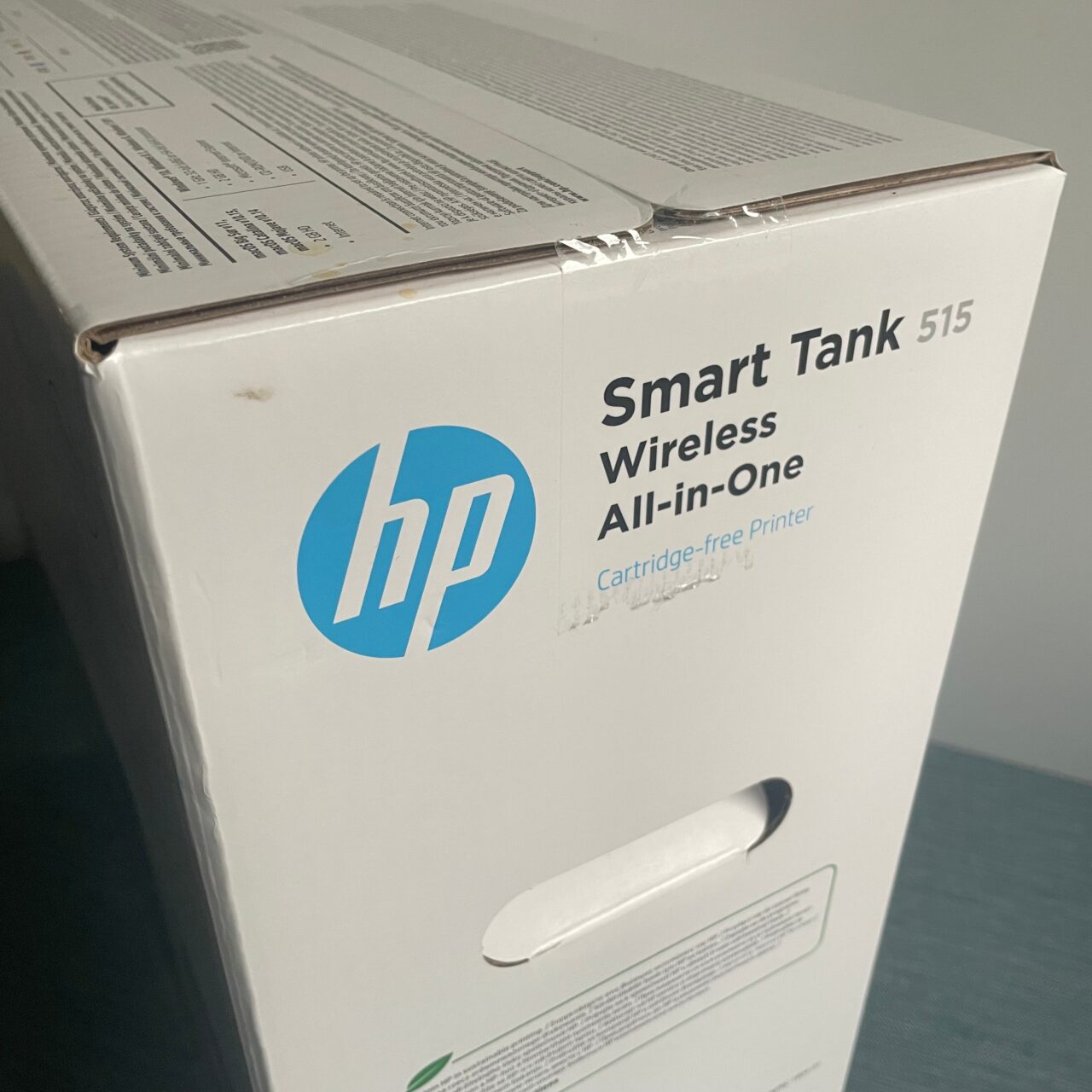 Kartonowe opakowanie drukarki HP Smart Tank 515 Wireless All-in-One z zamazanym tekstem i lekko zniszczonym rogiem.
