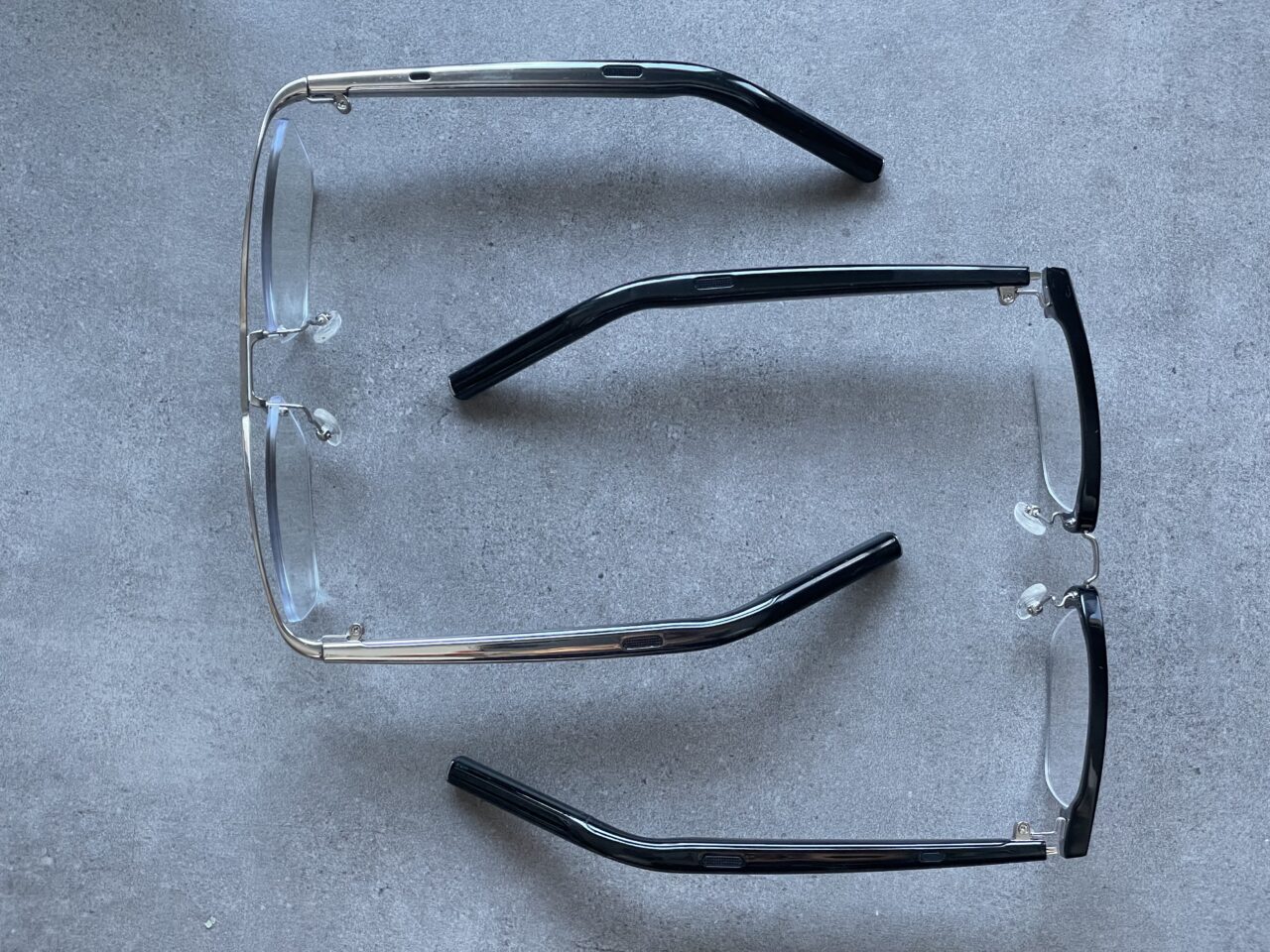 Dwa rozbite okulary z przezroczystymi szkłami na szarym tle, ich oprawki są połamane i rozłożone na dwie części.