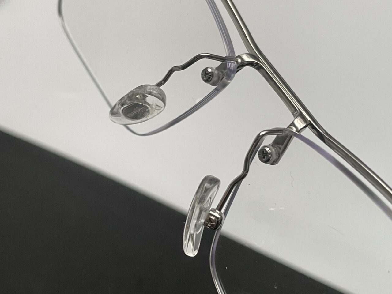 Zbliżenie na przezroczyste okulary z metalową oprawką leżące na białej powierzchni.