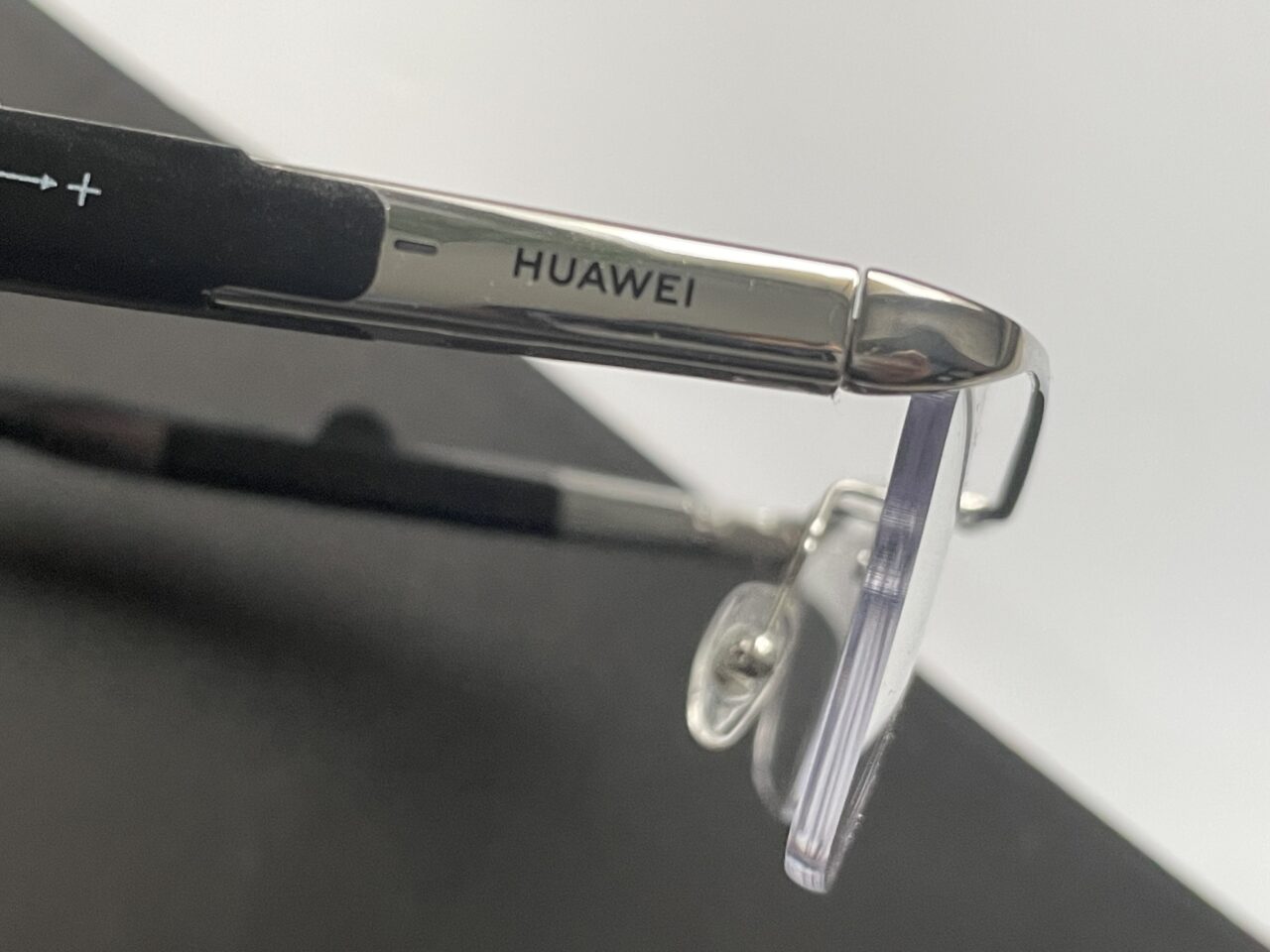 Zbliżenie na srebrną obręcz okularów z logo marki Huawei, położone na czarnej powierzchni.