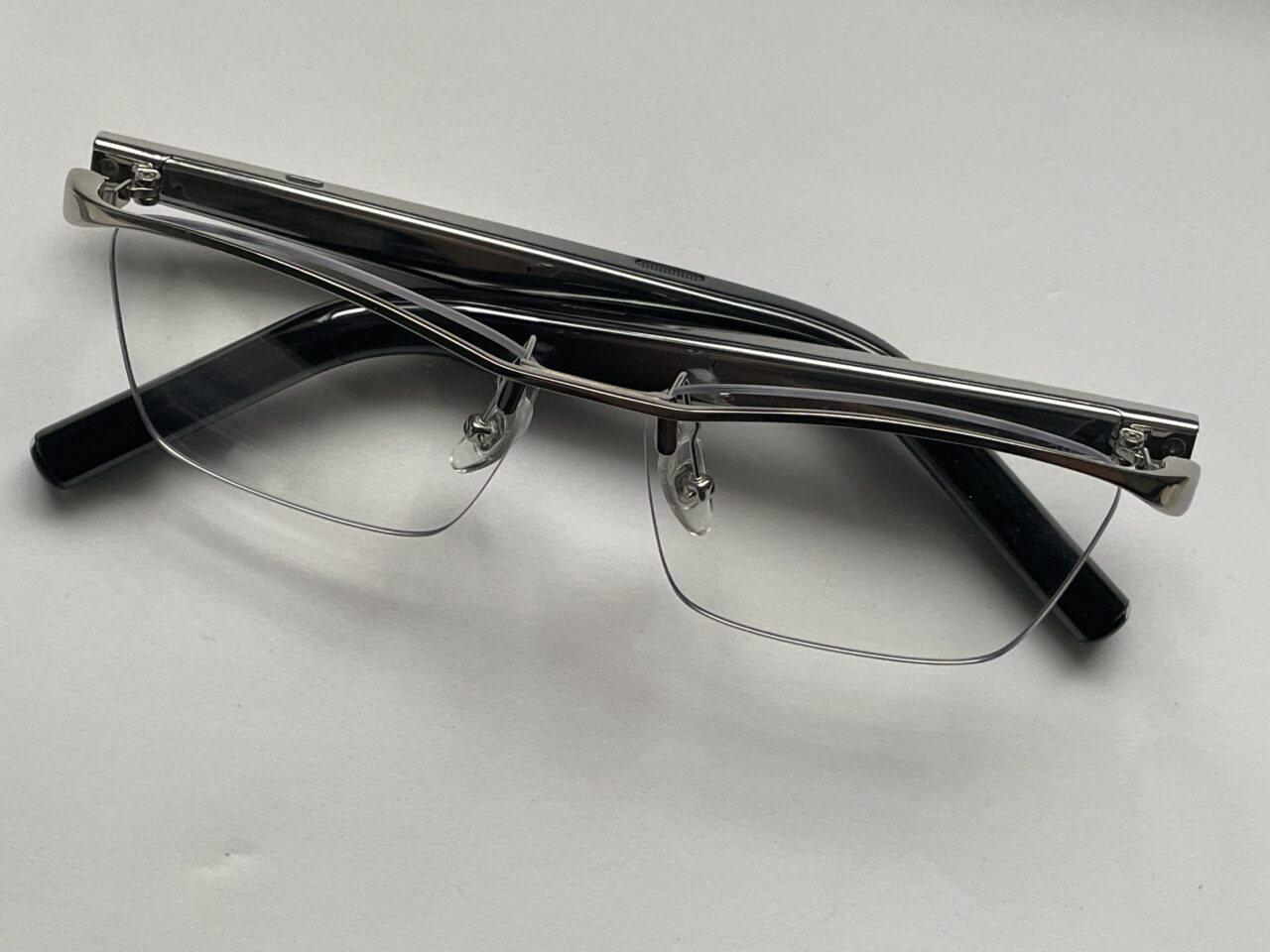 Czarne, półramkowe okulary korekcyjne z przezroczystymi soczewkami, leżące na białym tle.